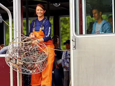 A woman in an orange jumpsuit holding a basket of crab